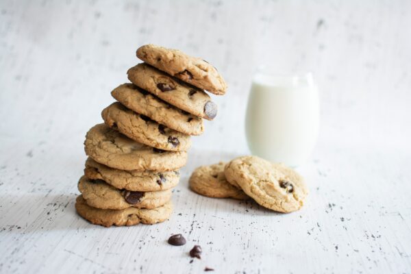 Tower of chocolate chip cookies leaning over, with a glass of milk and two other cookies in the background