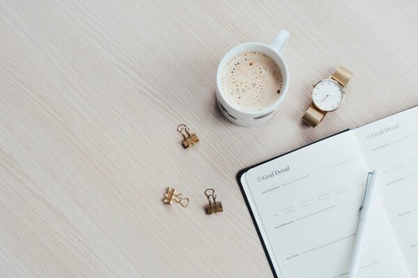 A coffee, watch, clips and and journal on a wood desk