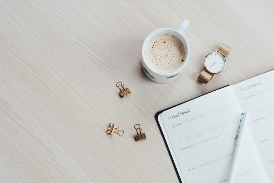 A coffee, watch, clips and and journal on a wood desk